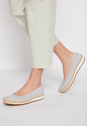 Chaussures compensées gris clair à enfiler avec bordure tissée et semelles blanches portées avec un pantalon court de couleur claire.