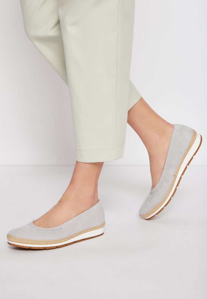 Chaussures compensées gris clair à enfiler avec bordure tissée et semelles blanches portées avec un pantalon court de couleur claire.