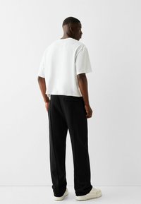 White cropped t-shirt with a relaxed fit, paired with black loose-fitting pants featuring side pockets and black accents.
