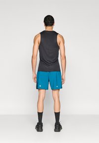 Μαύρο αμάνικο μπλουζάκι με στρογγυλή λαιμόκοψη, συνδυασμένο με τιρκουάζ σορτς που έχουν δύο λευκές κουκκίδες. Φορεμένο με μαύρες κάλτσες και αθλητικά παπούτσια.