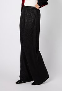 Czarne spodnie o szerokich nogawkach z subtelnym wzorem w panterkę, elastycznym paskiem w talii oraz gładką, miękką fakturą.