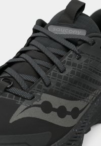 Černé tenisky Saucony s šedými vzorovanými tkaničkami, texturovaným síťovým svrškem a tečkovaným detailem podešve.