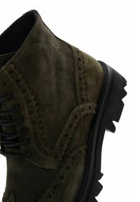 Botines de ante verde con detalles de brogue, punta redonda, cordones negros y suela de goma gruesa. Presenta una superficie texturizada y un intrincado bordado.