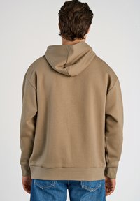 Sudadera con capucha de color marrón claro y corte holgado, con puños y dobladillo acanalados. Textura suave con un diseño simple y sin adornos.