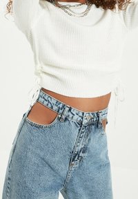 Haut blanc à manches longues côtelé avec cordons latéraux associé à un jean en denim bleu clair taille haute avec des découpes uniques.