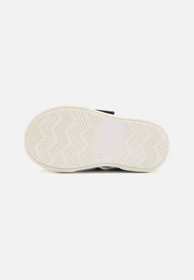 Schwarzer Sneaker mit einer weißen Gummisohle, die ein Zickzack-Profilmuster aufweist. Die Unterseite zeigt eine glatte Textur und die Größe ist mit "21" bedruckt.