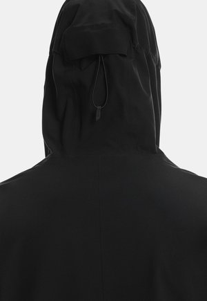 Melna kapucēta jaka ar brīvu siluetu, mīkstu audumu, savelkamu auklu un smalku izšuvuma detaļu aizmugurē.