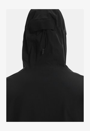 Melna kapucēta jaka ar brīvu siluetu, mīkstu audumu, savelkamu auklu un smalku izšuvuma detaļu aizmugurē.