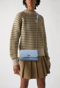 Borsa a tracolla trapuntata azzurro chiaro con patta, hardware in argento e tracolla a catena, abbinata a un maglione a righe in maglia e a una gonna plissettata.