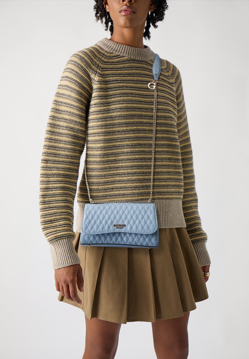 Borsa a tracolla trapuntata azzurro chiaro con patta, hardware in argento e tracolla a catena, abbinata a un maglione a righe in maglia e a una gonna plissettata.