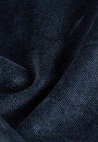 Tmavě modrá látka s měkkým, texturovaným povrchem. Materiál má jemné linie a subtilní lesk, což vytváří bohatý, sametový vzhled.