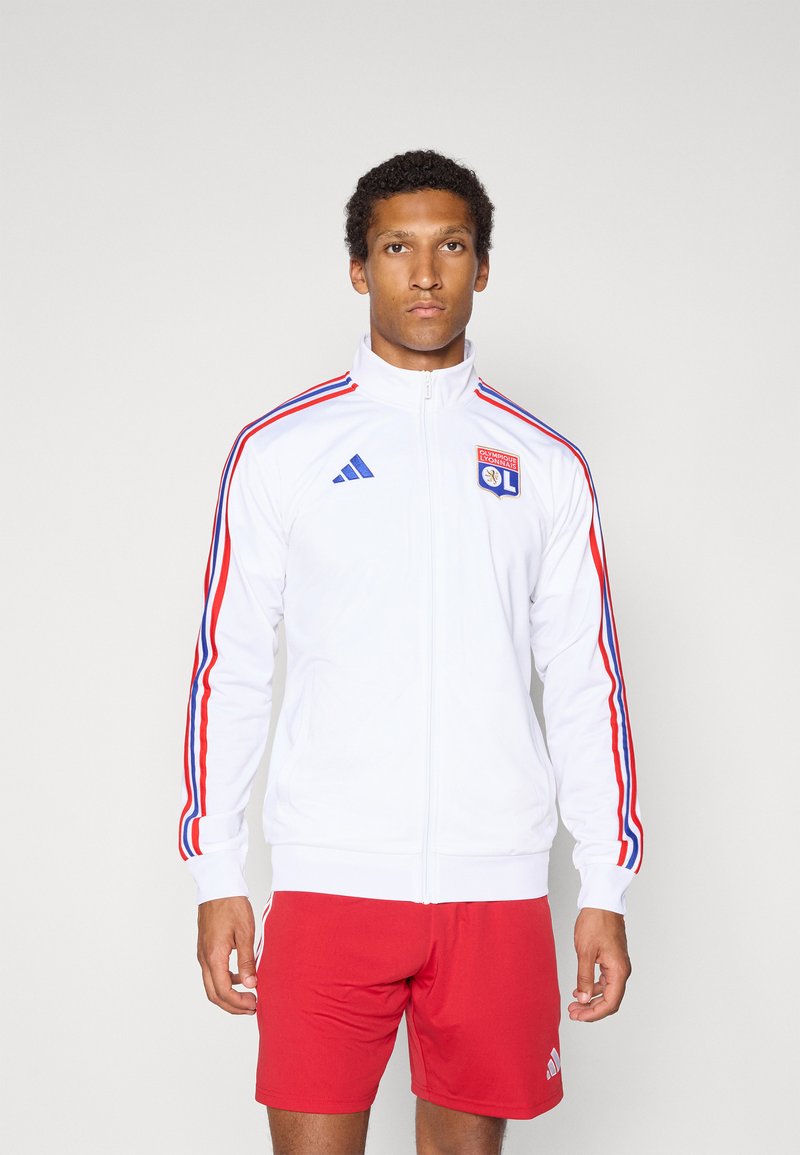 Weiße Zip-Jacke mit blauen und roten Streifen an den Ärmeln, mit gesticktem Logo. Getragen mit roten Shorts für Sportbekleidung.
