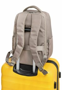 Beżowy plecak z wyściełanymi paskami i górnym uchwytem, zabezpieczony na teksturowanej żółtej walizce z wysuwanym uchwytem.