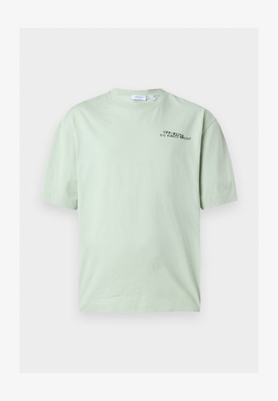 T-shirt vert clair à manches courtes avec texte noir « OFF-WHITE c/o VIRGIL ABLOH™ » sur le côté gauche de la poitrine.