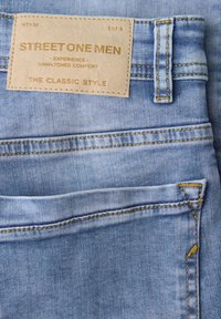 Poche de jean en denim bleu clair avec couture marron et étiquette en cuir beige portant la mention "STREET ONE MEN - EXPERIENCE UNMATCHED COMFORT - THE CLASSIC STYLE."
