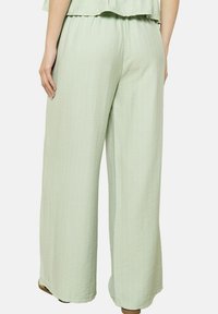 Svetlo zelene hlače širokega kroja, izdelane iz teksturirane tkanine z navpičnimi črtami. Elastičen pas, ohlapen kroj in preprost, minimalističen dizajn.