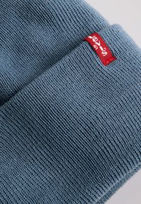 Blue knitted fabric with a ribbed texture. Features a small red tag with white lettering. Fabric appears soft and flexible.