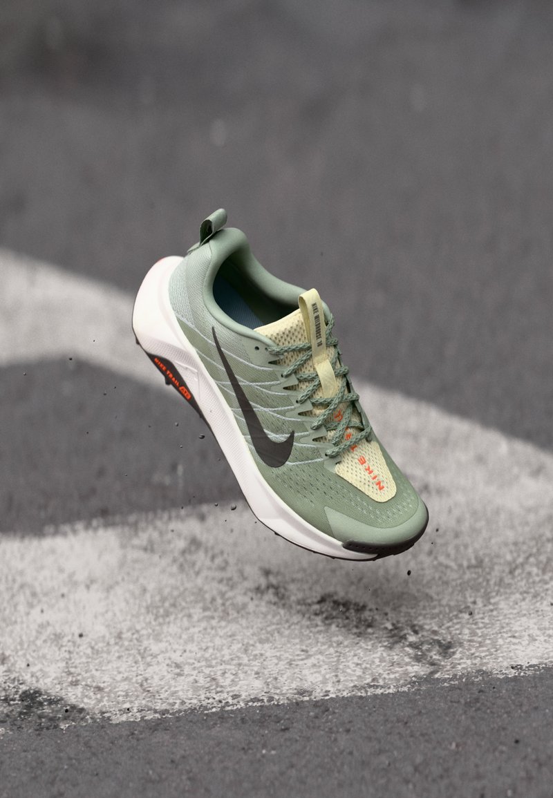 Svetlozelené bežecké topánky s textilným zvrškom, sivý logo Nike a biela podrážka, so zvýrazneniami a šnúrkami v oranžovej farbe. Ľahký dizajn pre optimálny výkon.