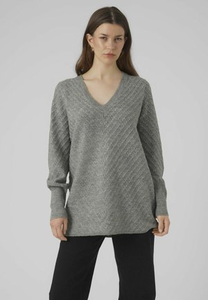 Grauer V-Ausschnitt-Pullover mit strukturiertem Chevron-Muster, langen Ärmeln und lockerer Passform, kombiniert mit schwarzen Hosen.