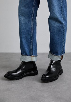 Zwarte leren enkellaarzen met elastische zijpanelen en gestructureerde rubberen zolen, gecombineerd met opgerolde blauwe denim jeans.