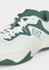 Λευκό και πράσινο sneaker Emporio Armani EA7 με λευκά κορδόνια και υφή στη σόλα, εμφανίζεται σε πλάγια πλευρική όψη.