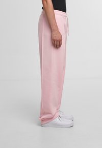 Light pink sweatpants with an elastic waistband and side pockets, featuring a straight leg design, paired with white sneakers.