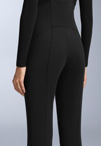 Černý body s dlouhým rukávem z elastické tkaniny. Má viditelné švy a přiléhavý střih, který zvýrazňuje kontury a siluetu.