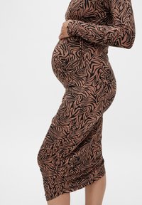 Gravidklänning i brunt med ett svart abstrakt zebramönster, med långa ärmar och en kroppsnära passform som accentuerar babymagen och har rynkor på sidan.