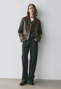 Brun læder cropped jakke med krave, med knapper og to frontlommer. Kombineret med mørke, lige ben jeans og sorte sko.