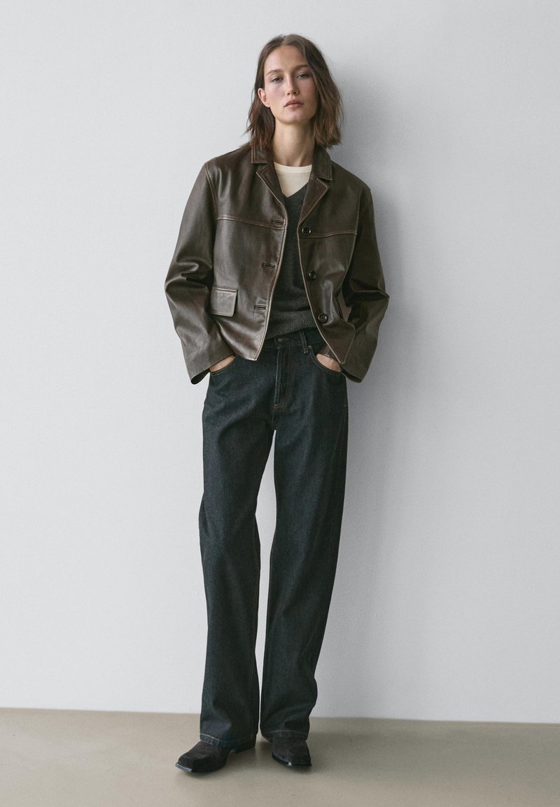 Brun læder cropped jakke med krave, med knapper og to frontlommer. Kombineret med mørke, lige ben jeans og sorte sko.