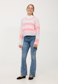 Sweter dzianinowy w pastelowych odcieniach różu i zieleni; wysoka szyja, luźny krój. Para jasnoniebieskich, rozszerzających się spodni cargo z kieszeniami.