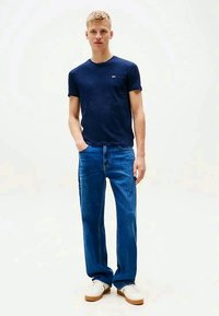 Nαυτικό μπλε βαμβακερό t-shirt συνδυασμένο με ανοιχτό μπλε τζιν. Το μοντέλο φοράει λευκά sneakers, αναδεικνύοντας μια άνετη εφαρμογή και κλασικό σχέδιο.