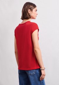 Top corto rosso a maniche corte con scollatura rotonda, realizzato in tessuto testurizzato, abbinato a denim blu. La vestibilità è comoda, con un design semplice.