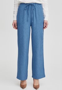 Pantaloni azzurri chiari, larghi e con tessuto in rilievo, dotati di un cinturino annodato in vita. Design a gamba dritta e cuciture minime.
