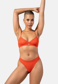 Bralette orange à dentelle suivie de son thong assorti, mettant en avant de délicats détails en dentelle, des bretelles fines et une texture de tissu lisse.