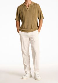Olivgrön stickad polo med V-ringning och korta ärmar, kombinerad med krämfärgade byxor och vita sneakers.