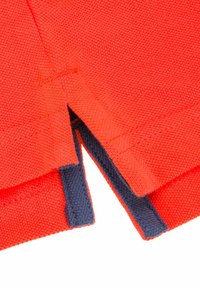 Czerwona bawełniana tkanina o teksturowanym splocie, z niebieskimi akcentami na brzegach i bocznymi rozcięciami, podkreślająca detale projektu i szycia.