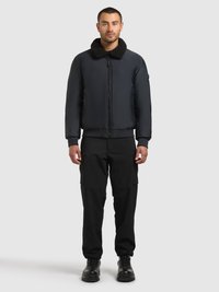 Laivastonsininen pommikoneen takki, jossa musta tekoturkiskaulus, edessä vetoketju ja sivutaskut, yhdistettynä mustiin cargo-housuihin ja tukevin mustiin saappaisiin.