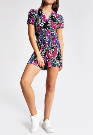 Jumpsuit negro de manga corta con un vibrante patrón floral y de leopardo, con cintura ajustada y un corte holgado, combinado con zapatillas blancas.