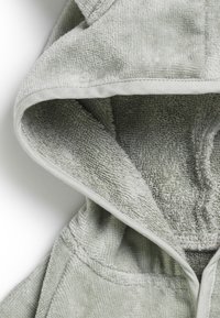 Ljusgrön huvtröja med ett mjukt, texturerat tyg. Har en kontrasterande kant längs huven och en ficköppning fram.