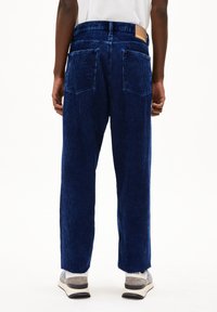 Blauwe corduroy wijde broek met verticale ribbels, twee achterzakken en een leren label op de tailleband. Gekenmerkt door grijze sneakers.