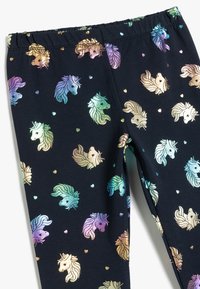 Leggings aus marineblauem Stoff mit einem wiederholten Muster von holografischen Einhornköpfen und kleinen Herzen in verschiedenen Pastellfarben.