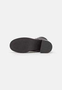 Stivaletto nero con suola in gomma testurizzata, punta rotonda e dettaglio a risvolto. Presenta una tomaia in pelle liscia e un accentuato contrasto del tacco.