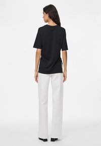 Sort kortærmet T-shirt med en afslappet pasform, der har rund halsudskæring og sideslids, kombineret med hvide højtaljede bukser.