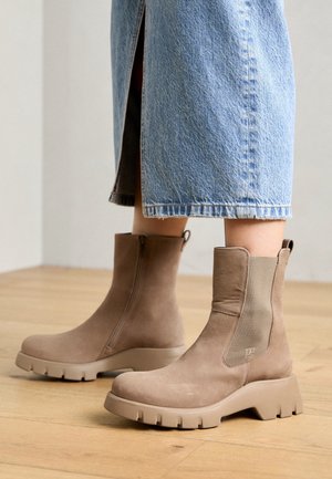 Brune ankelstøvler med en glat ruskindsoverflade, sidelås og en kraftig gummisål. Kombineret med et lyst denimplast.