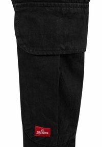 Schwarze Cargo-Hosen aus strapazierfähigem Material, mit einer Klapptasche und einem roten Markenpatch am Unterschenkel. Glatte Textur, gerades Design.