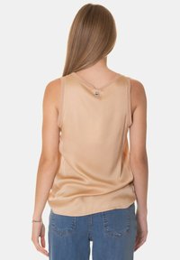 Top senza maniche color beige chiaro realizzato in tessuto liscio, caratterizzato da un collo a V e un'etichetta sul retro. Abbinato a jeans in denim blu.