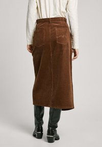 Falda midi de pana marrón con dos bolsillos traseros, acanalado vertical y una cintura ajustada, combinada con botas negras ajustadas.