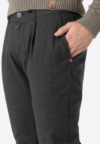 Grau gemusterte Hose mit einem dezenten Karodesign, flacher Vorderseite, Seitentaschen und einem Knopfdetail an der Tasche.