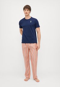 Mornarsko plavi pamučni majica s malim izvezenim uzorkom, uparen s laganim pidžama hlačama narančasto-bijelih pruga.